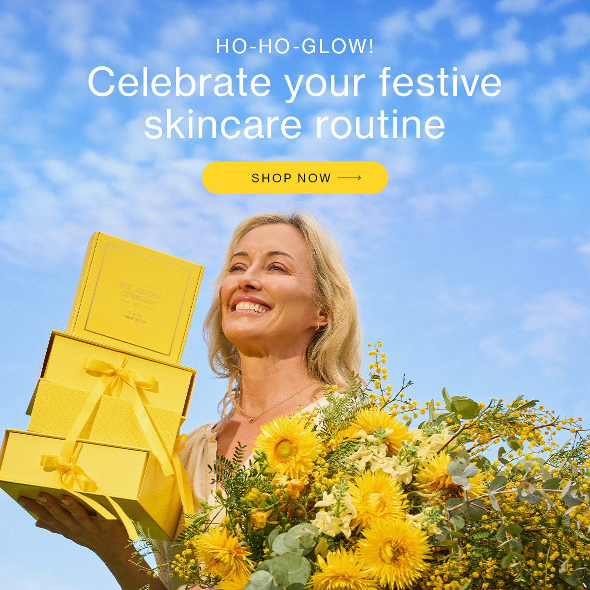 Person holding yellow gift boxes with text about skincare routine and shop now button against a blue sky.